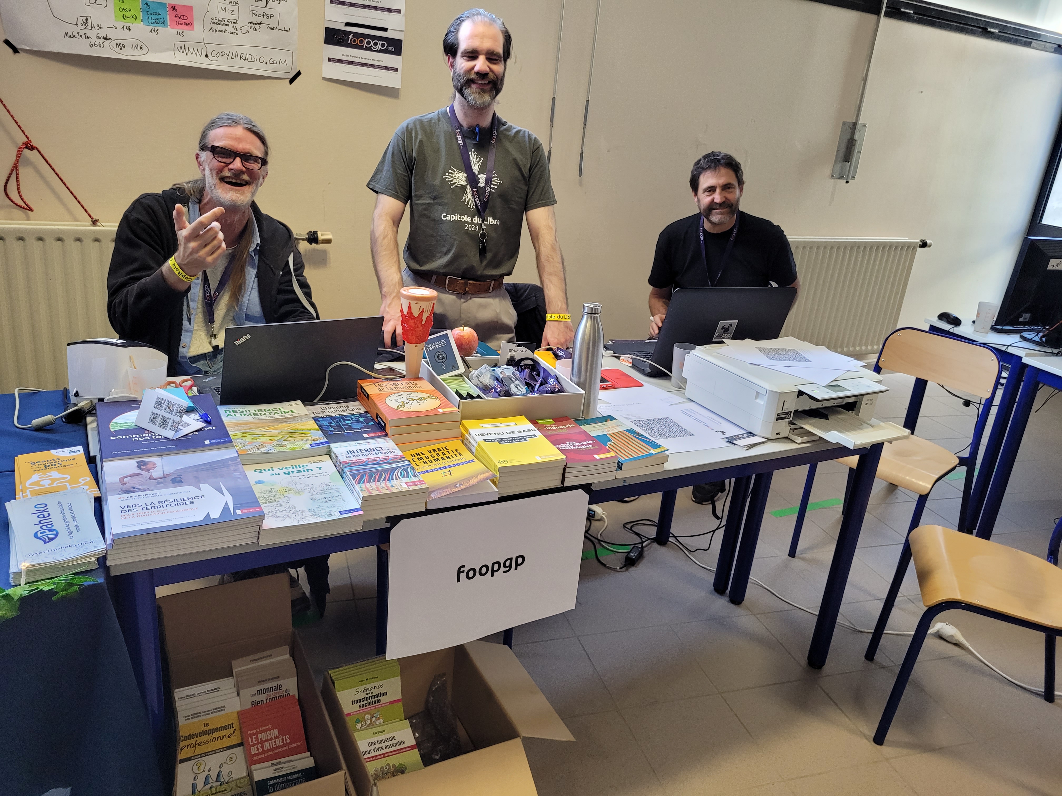 3 smiling foopgp members behind the association’s stand at the capitole du libre (2024-11-16 Toulouse)